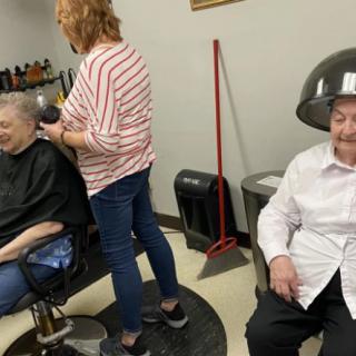 Elderly women enjoying a salon day, one getting her hair styled and another under a hairdryer.