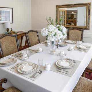 A beautifully set dining table with elegant dishware and a floral centerpiece in a well-decorated dining room.