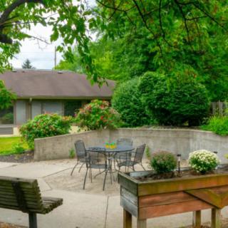 A tranquil garden patio with lush greenery, featuring a seating area with a table and chairs.