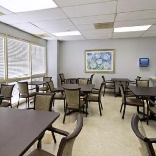 An empty cafeteria with several tables and chairs, large windows, and a piece of artwork on the wall.