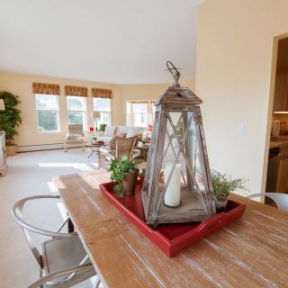 A cozy dining area with a decorative lantern and plants centerpiece on a wooden table, illuminated by natural light.