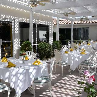 A beautifully set outdoor dining area with tables adorned with yellow napkins under a pergola.