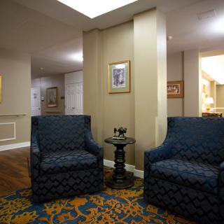 A cozy lobby area with two armchairs, a small table, artwork on the walls, and a decorative carpet.