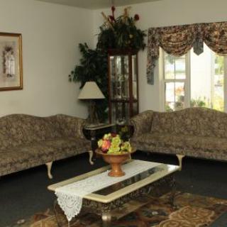 A classic living room featuring patterned sofas, a glass coffee table with a fruit centerpiece, and decorative curtains.