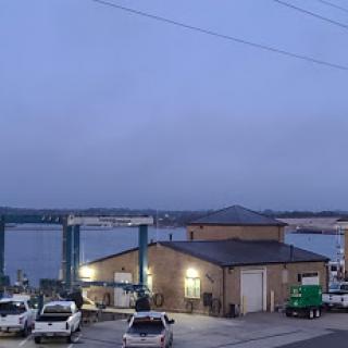 A quiet harbor scene at dusk, featuring a range of vehicles and a building near the water.