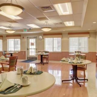 An empty dining room with elegantly set tables and chairs, featuring large windows and ceiling lights.