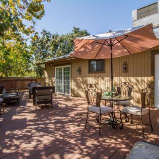 A sunny patio with outdoor seating and an umbrella, surrounded by trees.