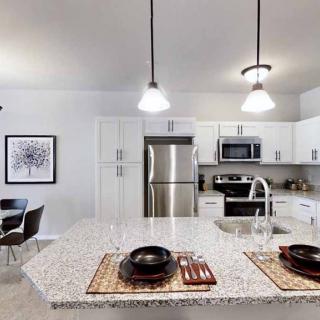 A modern kitchen with stainless steel appliances and a central island, featuring pendant lighting and adjacent dining area.