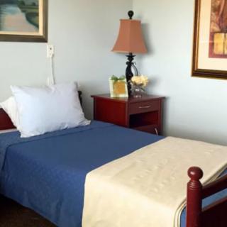 A cozy bedroom with a single bed, blue bedding, and a nightstand featuring a lamp and decor.