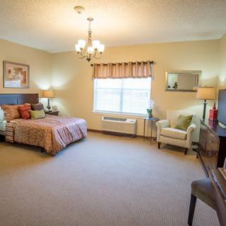A spacious and well-lit bedroom with a large bed, chairs, and decorative elements.