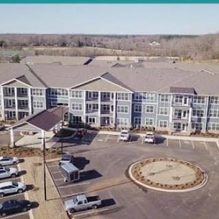 Aerial view of a modern residential building with ample parking and scenic surroundings.