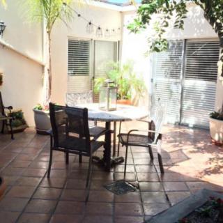 A cozy outdoor patio with a round table and chairs surrounded by potted plants and sunlight.
