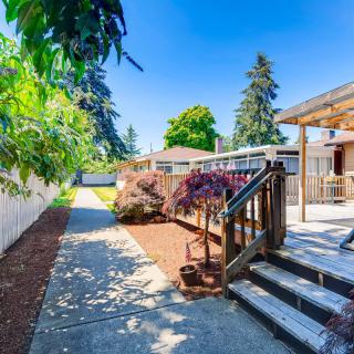 A sunny backyard featuring a wooden deck, a landscaped garden, and a pathway lined with trees and shrubs.