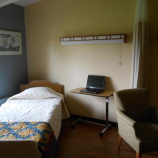 A cozy bedroom featuring a single bed, a desk with a laptop, and a comfortable chair, providing a functional yet inviting space.