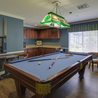 A cozy billiard room featuring a pool table, cue sticks, and a stained glass hanging light.