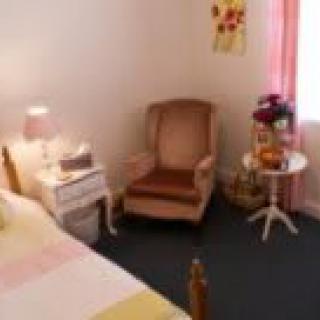 A cozy bedroom with a comfortable armchair, a nightstand with a lamp, and floral decorations.