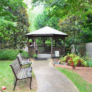A tranquil garden setting featuring a gazebo, benches, and a pathway surrounded by lush greenery and colorful flowers.