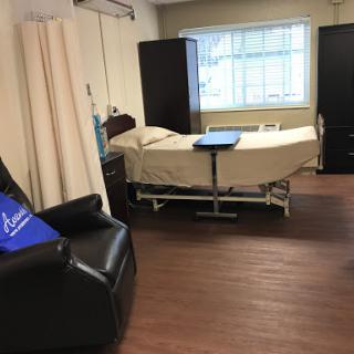 A view of a hospital room featuring a patient bed, a chair, and natural light coming through the window.