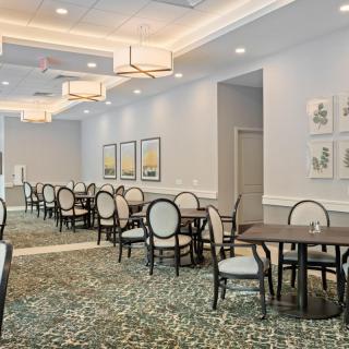 A spacious dining room with neatly arranged tables and chairs, decorated with elegant artwork and bright lighting.