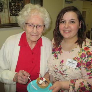 An elderly woman and a young woman smiling together while celebrating with cake.
