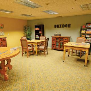 A cozy library reading room with tables, chairs, and bookshelves.
