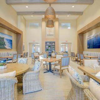 A spacious dining area with wicker chairs, round tables, and artwork on the walls.