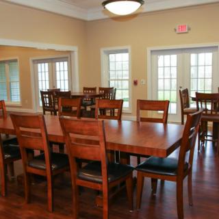 A spacious dining room with wooden tables and chairs, featuring large windows and ambient lighting.