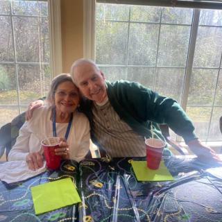 A couple sitting together at a table indoors, holding drinks and enjoying each other's company.