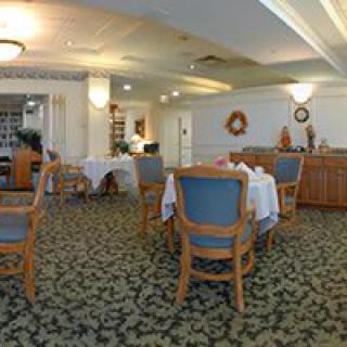 A cozy dining room with neatly arranged tables and chairs, featuring elegant decor and a carpeted floor.