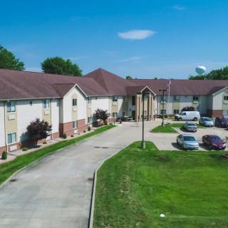 A residential building with a driveway and parking lot surrounded by grass and trees.