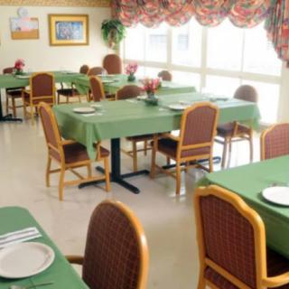 A decorated dining room with tables and chairs arranged neatly, featuring green tablecloths and place settings.