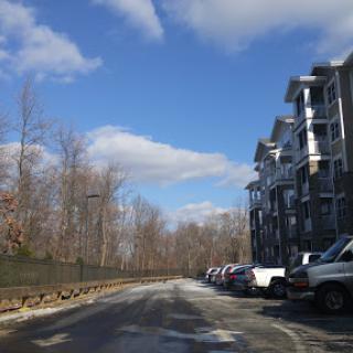 A peaceful urban street lined with apartments and parked cars, under a clear blue sky with scattered clouds.