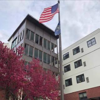 A modern building with an American flag and state flag, surrounded by blooming pink trees.