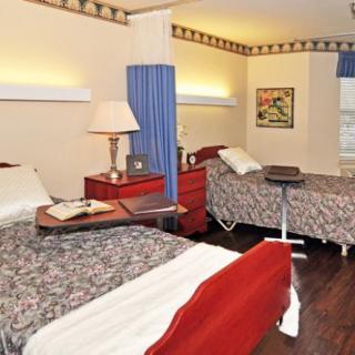 A hospital room with two beds, separated by a curtain, featuring medical equipment and a nightstand with a lamp.