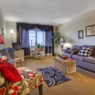 A cozy living room featuring comfortable seating, colorful decor, and a large window bringing in natural light.