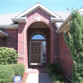 Front entrance of a brick house with a wooden door and surrounding greenery.