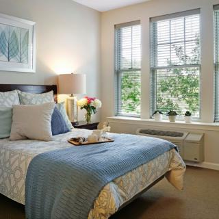 A cozy bedroom with a neatly made bed, large windows, and inviting decor.