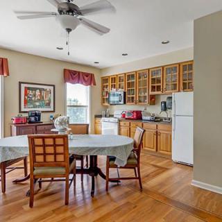 A cozy kitchen and dining area with wooden floors, equipped with a ceiling fan, table and chairs, cabinetry, and appliances.