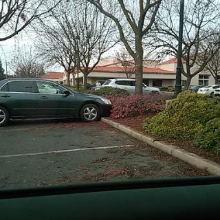 A car parked improperly on the edge of a parking lot, encroaching on the sidewalk.