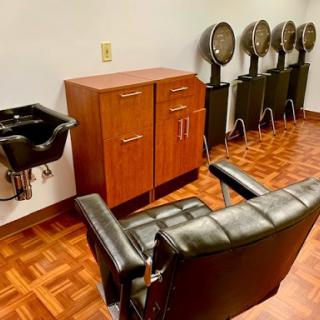 A hair salon interior featuring a styling chair, hair dryers, and a sink.