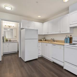 A modern kitchen featuring white cabinetry and appliances, complemented by warm wood flooring.
