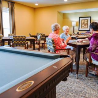 A group of seniors socializing in a recreation room with a billiards table.
