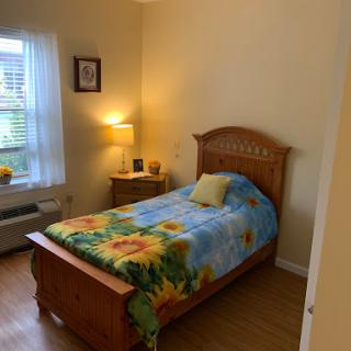 A cozy bedroom featuring a single wooden bed with floral bedding and a bedside lamp, creating a warm and inviting atmosphere.