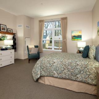 A cozy bedroom with a large bed, desk, and window letting in natural light.