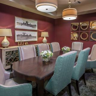 A modern dining room with a large wooden table, surrounded by upholstered chairs and decorated with ambient lighting and wall art.