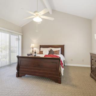 A cozy bedroom with a wooden bed frame, carpeted floor, and a ceiling fan.