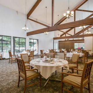 A spacious dining area with wooden tables and chairs, featuring exposed ceiling beams and chandeliers.