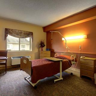 A well-lit hospital room featuring a bed and medical equipment, with furniture and a window view.
