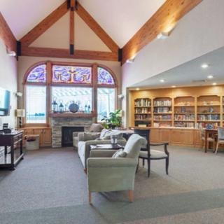 A cozy library with comfortable seating, bookshelves, a fireplace, and a stained glass window.
