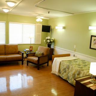 A well-lit and spacious hospital room featuring comfortable seating and a neatly made bed.